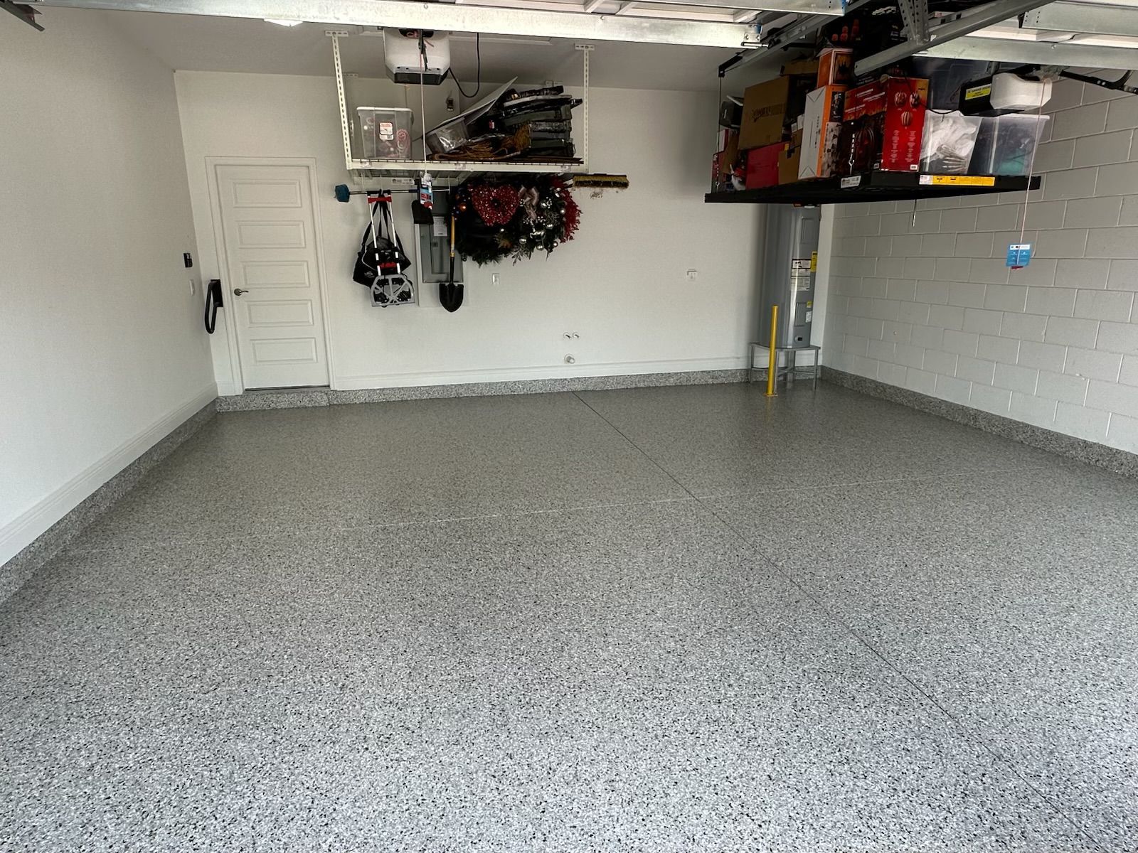 Empty garage with speckled floor, white walls, and storage shelves near the ceiling