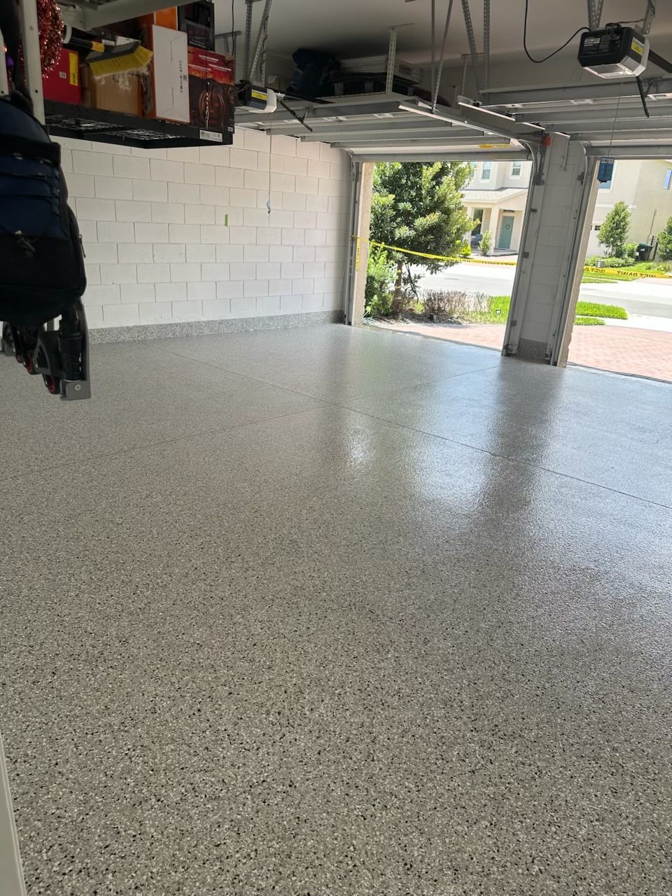 Empty garage with speckled gray floor, white walls, and open door to driveway outside.
