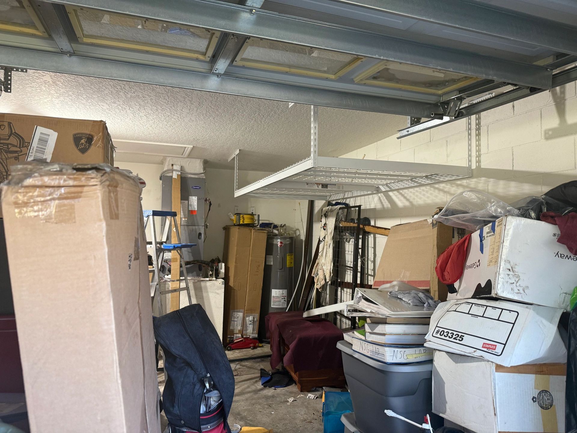 Cluttered garage with stacked boxes, bins, and tools under a metal ceiling.