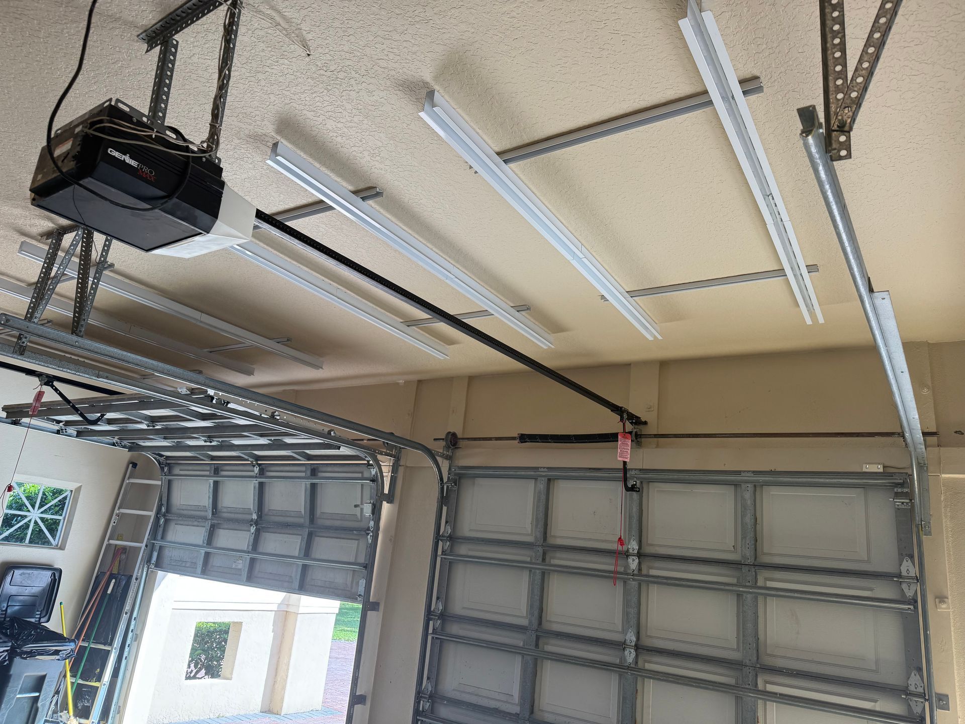 Garage interior with open door, ceiling-mounted fluorescent lights, and overhead garage door tracks