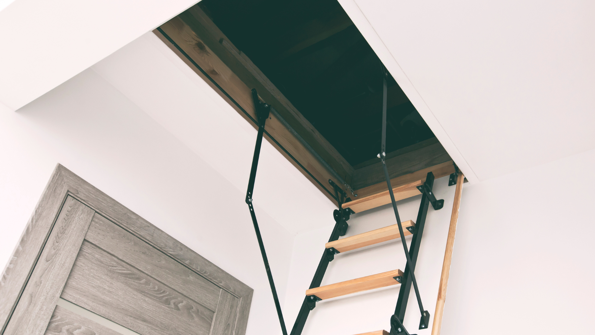 Open attic hatch with folding ladder in a white room