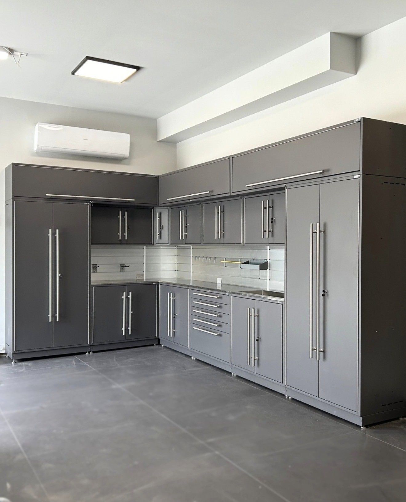 Modern gray garage cabinetry with stainless handles in a bright room, viewed from a corner.
