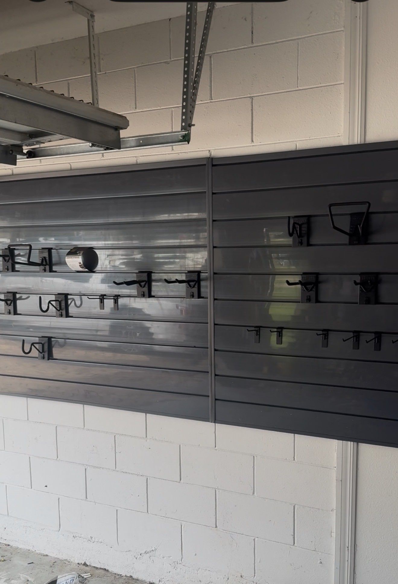 Gray slatwall display with hooks mounted on a white brick wall in a garage or workshop