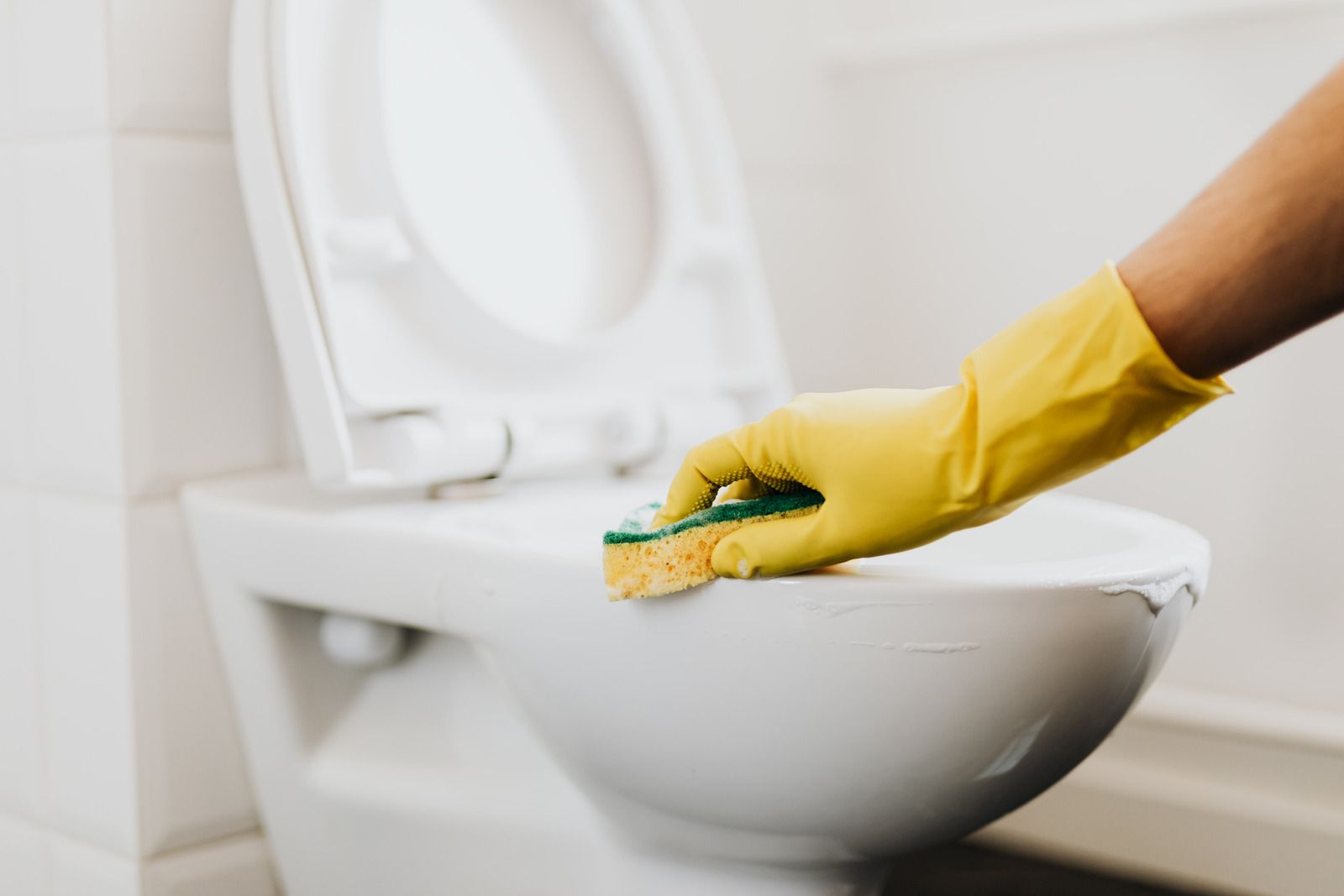 Yellow-gloved hand scrubbing a toilet bowl with a sponge in a bathroom