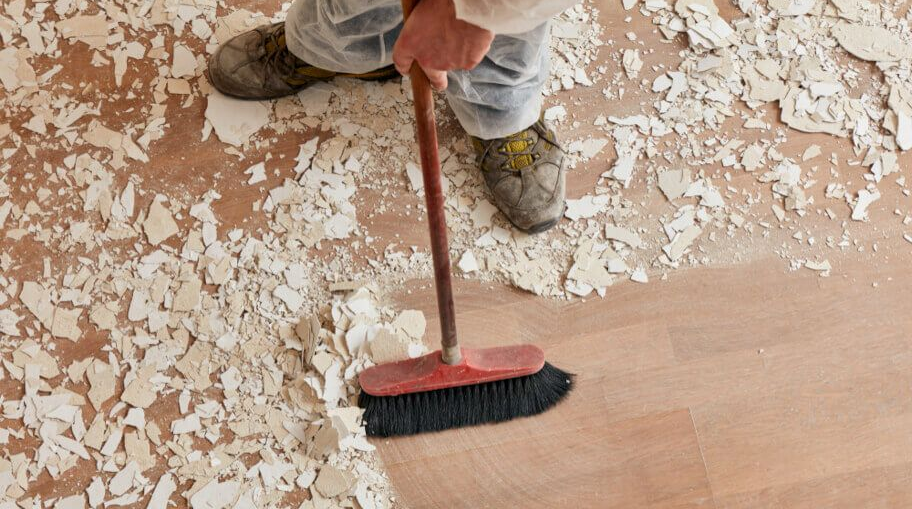 Person sweeping white paint flakes from a wooden floor with a broom.