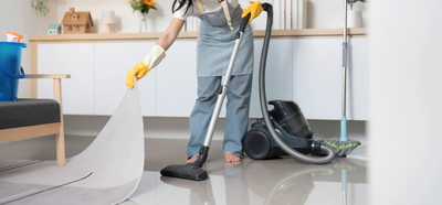 Person mopping a glossy floor beside a vacuum cleaner in a bright room