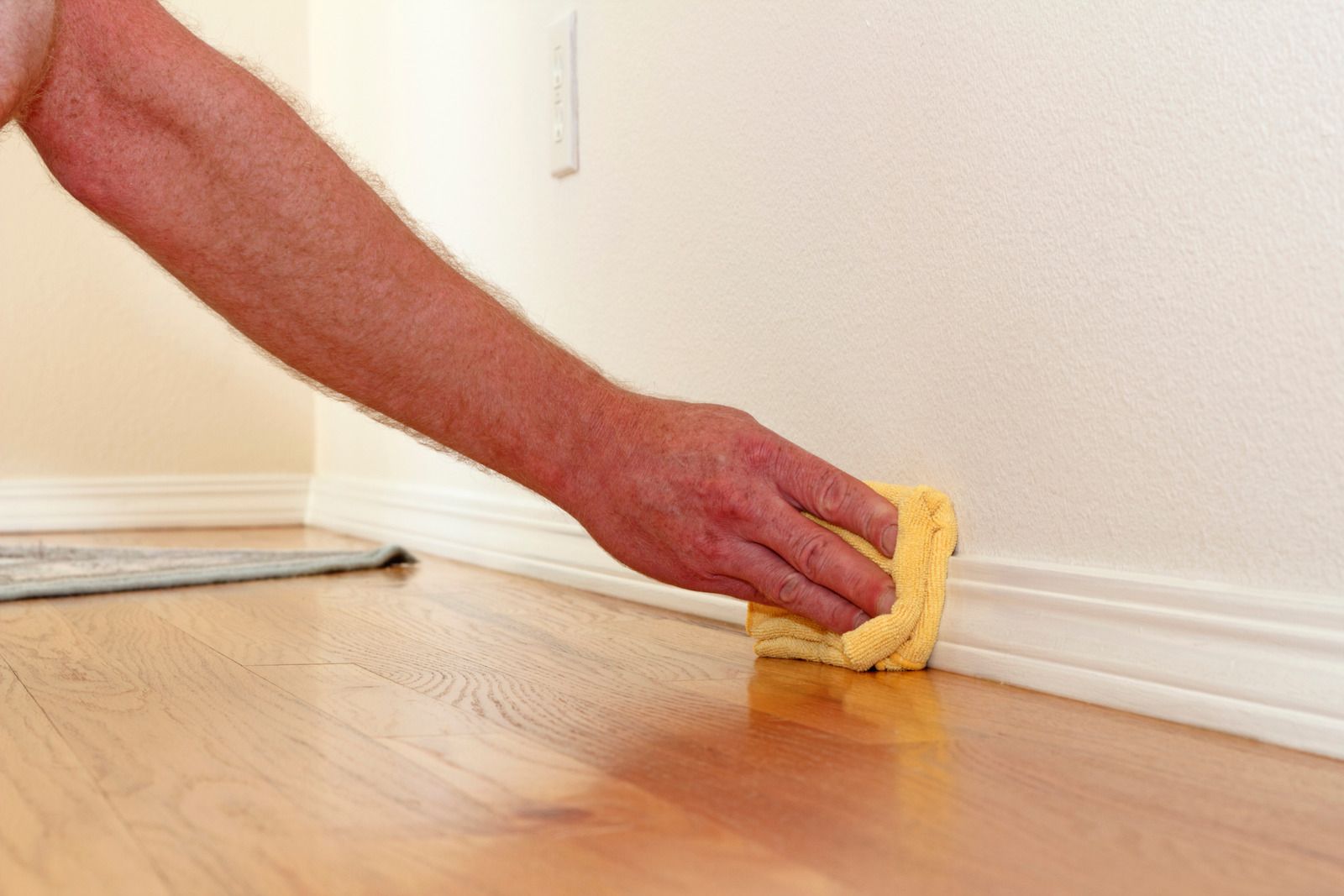 Hand wiping baseboard with yellow sponge on a hardwood floor