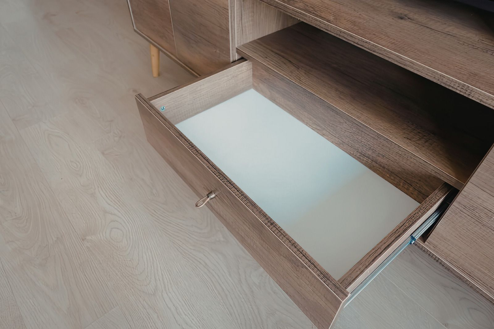 Open drawer in a wooden cabinet, showing a white interior shelf.