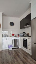 Modern kitchen with white cabinets, stainless steel appliances, dark wood floor, and a clock on the wall