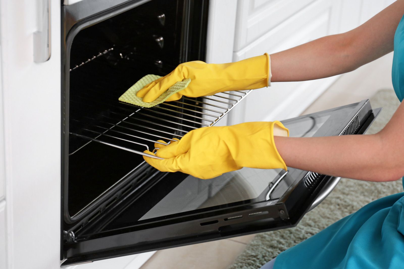 Person in yellow gloves cleaning the inside of an oven with the door open