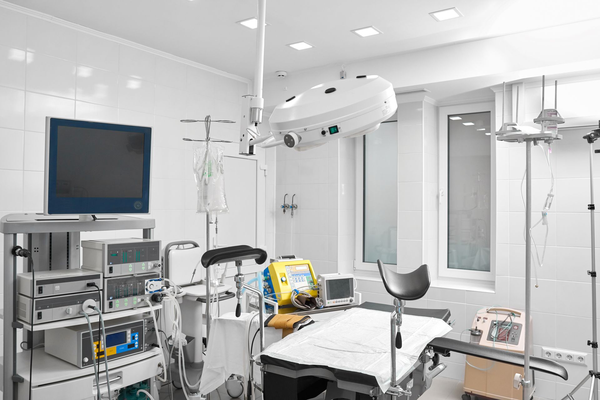 Sterile hospital operating room with surgical table, monitors, IV stand, and ceiling-mounted equipment Sterile hospital operating room with surgical table, monitors, IV stand, and ceiling-mounted equipment
