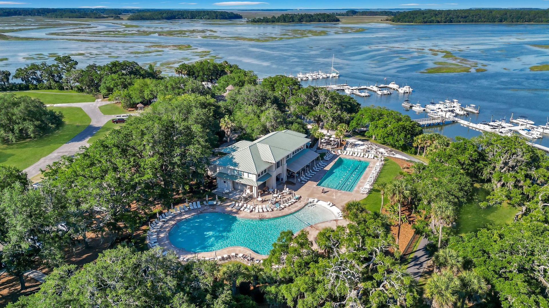 Aerial view of a resort with pools and marina beside a lush waterfront