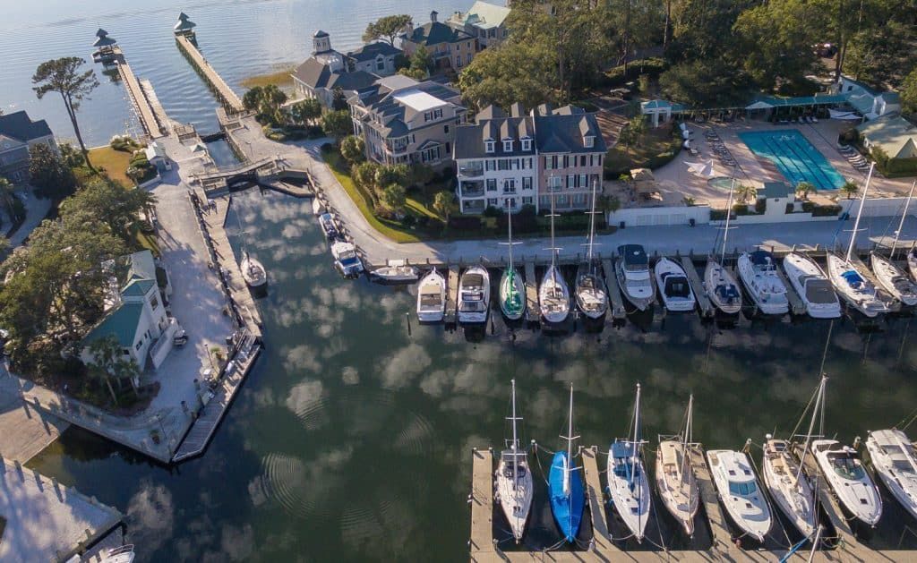 Aerial view of a marina with docked boats, waterfront houses, and a pool at sunset