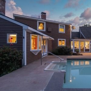 Backyard pool beside a two-story house at dusk, with warm lights glowing in the windows.