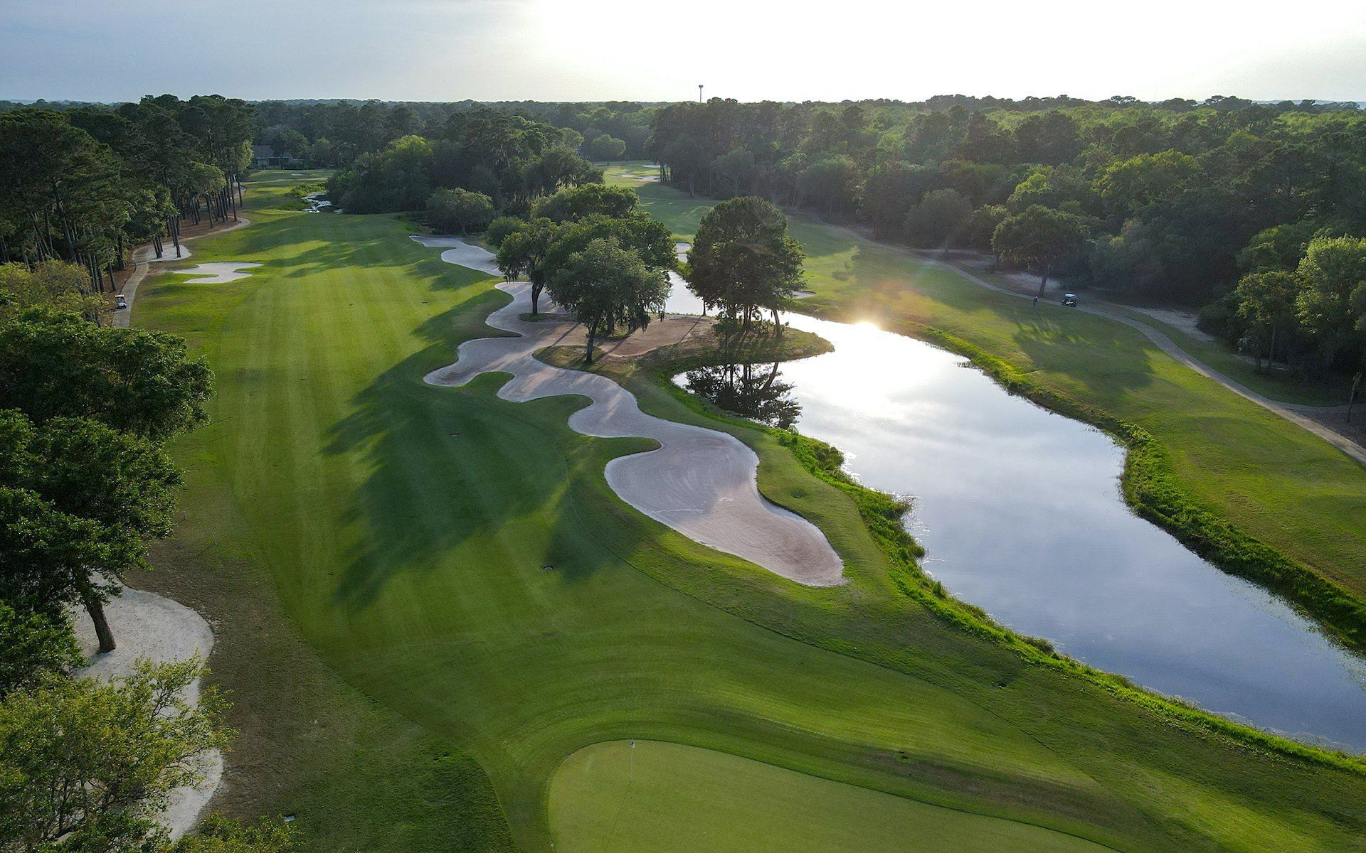 Aerial view of a golf course with green fairways, sand bunkers, and a water hazard at sunset