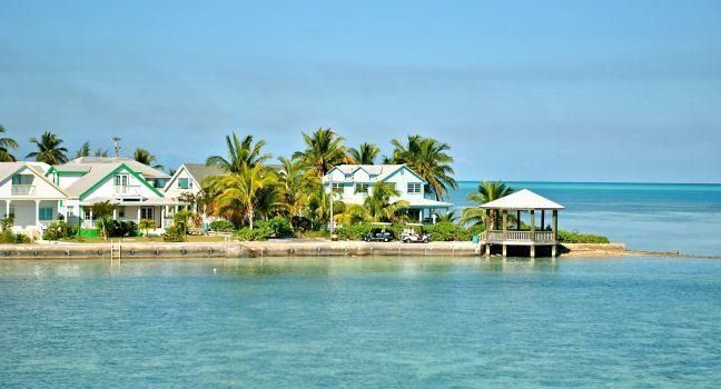 Tropical seaside resort with white houses, palm trees, a small dock, and calm blue water