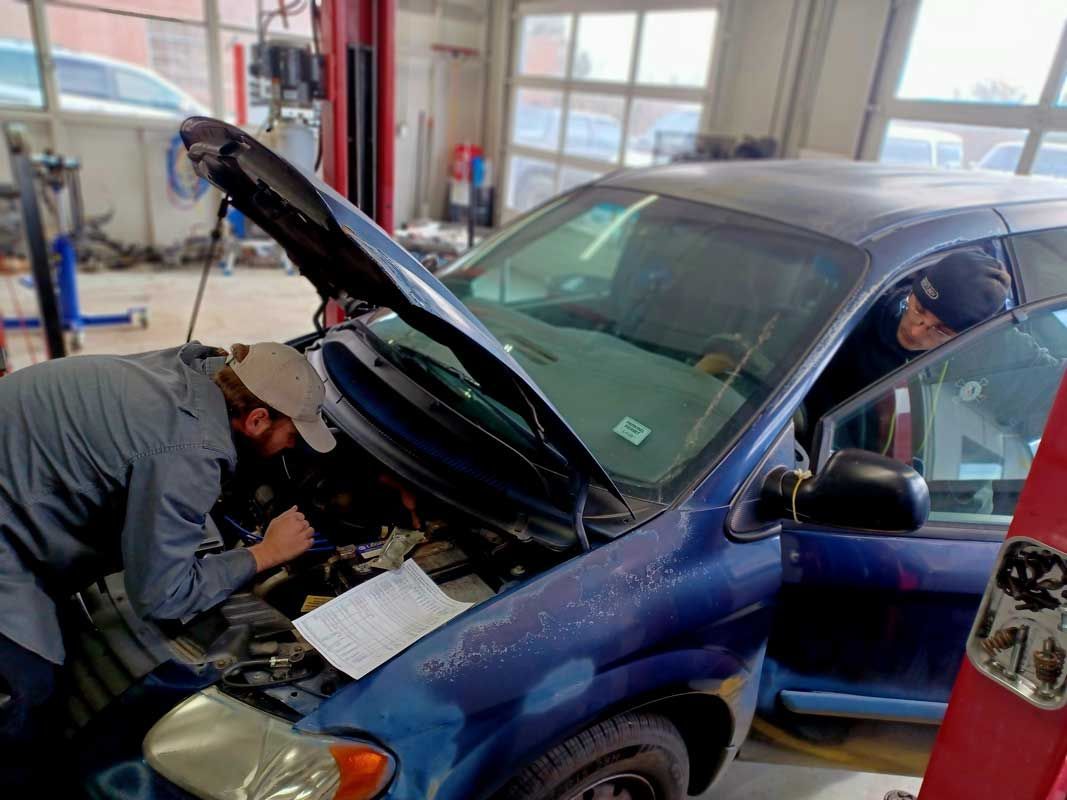 Mechanic inspecting a blue car with its hood open in a garage | Milestone Auto Repair LLC