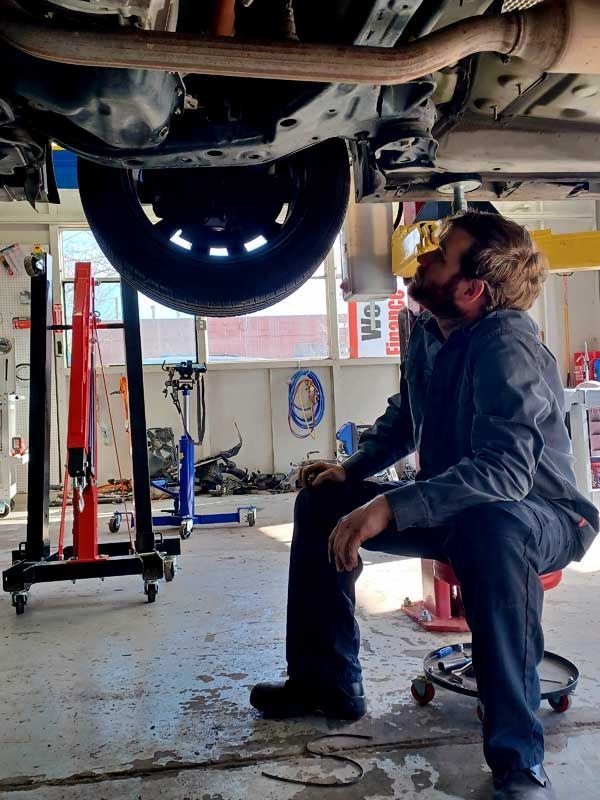 Mechanic inspecting the underside of a car on a lift in an auto repair garage | Milestone Auto Repair LLC