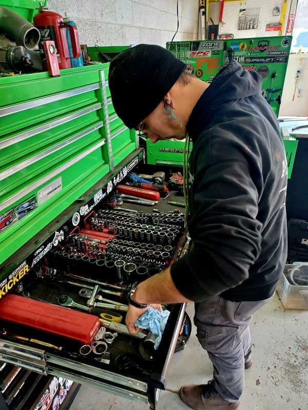 Mechanic leaning over an open green tool chest, searching through sockets and wrenches in a workshop | Milestone Auto Repair LLC