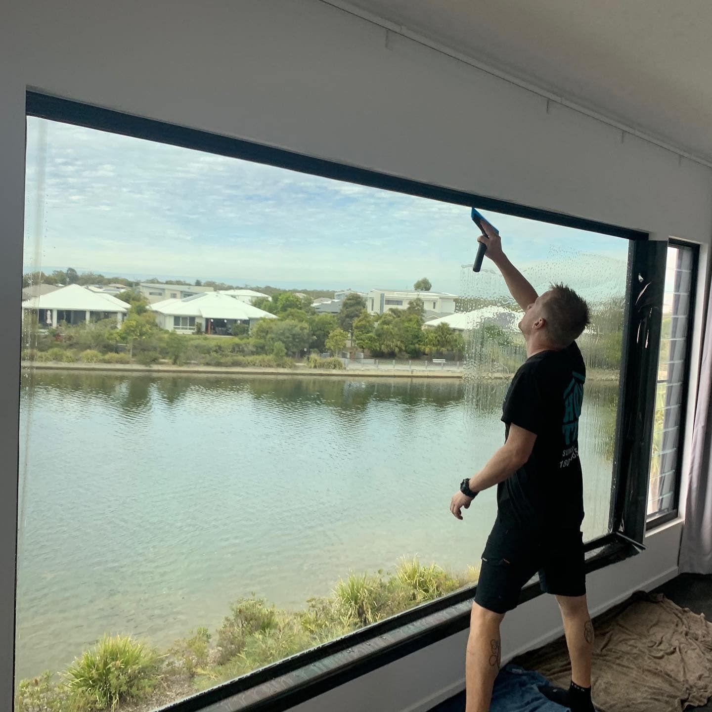 A Man Is Applying A Tint To Large Window Overlooking A Lake — Home Tint Sunshine Coast Window Tinting In Maroochydore, QLD