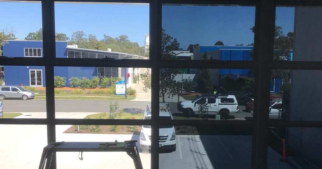 A View Of A Parking Lot Through A Window With A Blue Building In The Background — Home Tint Sunshine Coast Window Tinting In Maroochydore, QLD