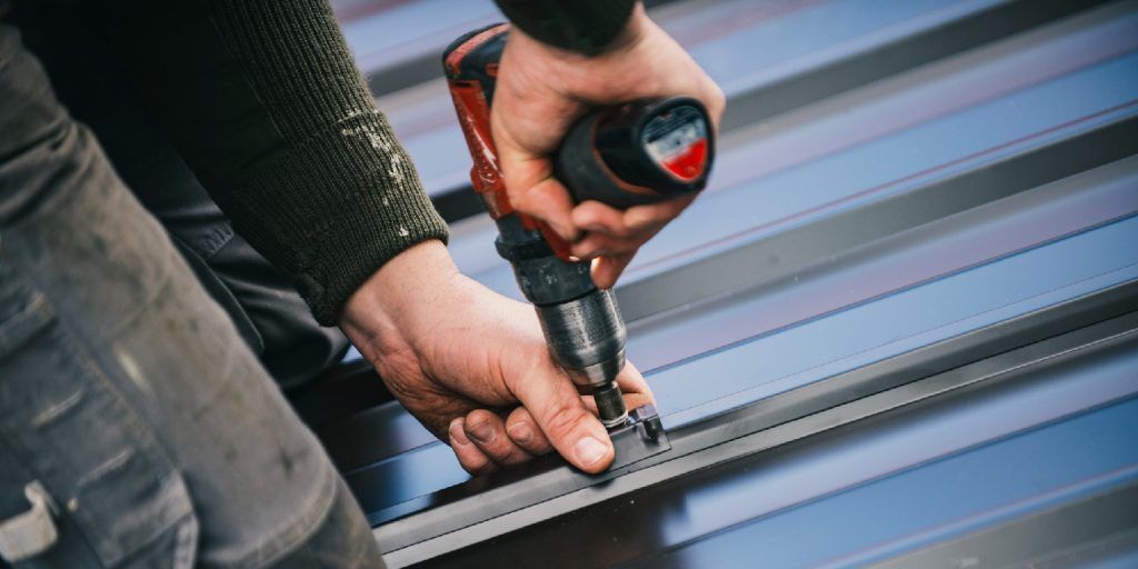 A Man Is Using A Drill On A Metal Roof — Home Tint Sunshine Coast Window Tinting In Maroochydore, QLD