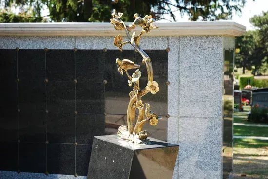 Abstract gold sculpture on a black pedestal in front of a white stone wall and dark glass doors
