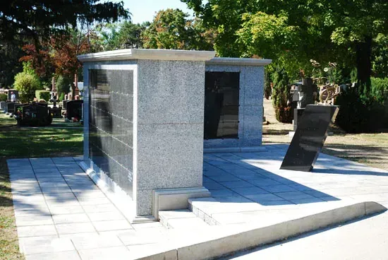 Stone memorial monument on a tiled plaza, with trees and benches in the background.