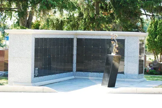 Modern outdoor memorial wall with dark panels and a black sculpture in front, surrounded by trees