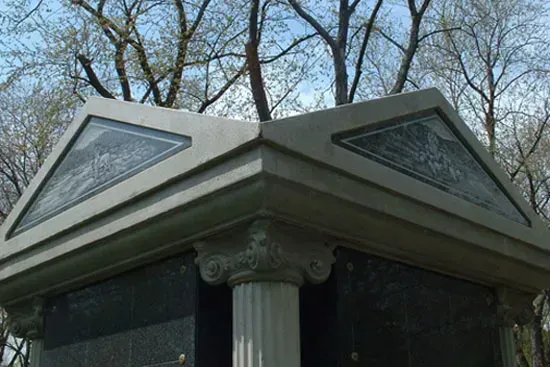 Corner of a mausoleum with a decorative roof and triangular windows, viewed among leafless trees