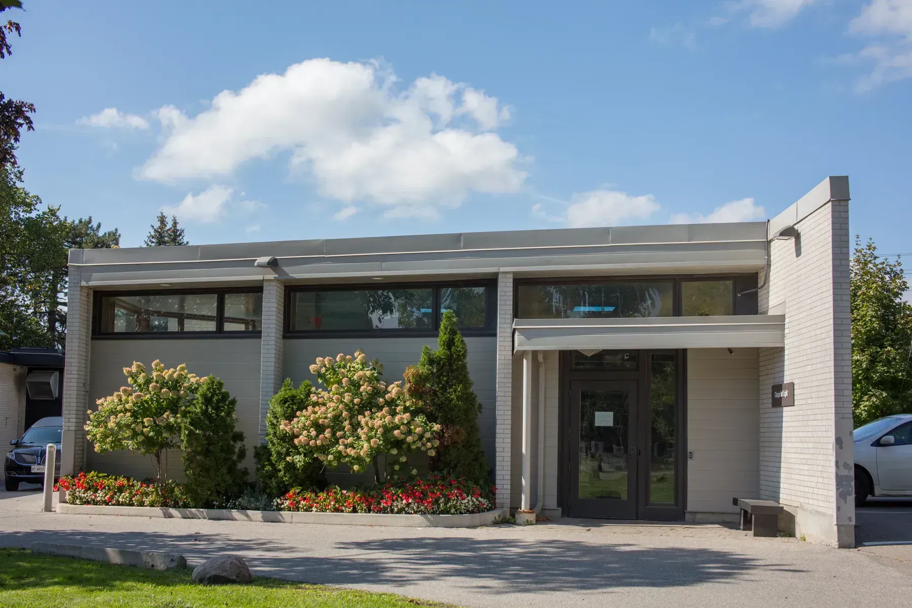 Modern gray office building with large windows, glass entrance, and shrubs under a blue sky