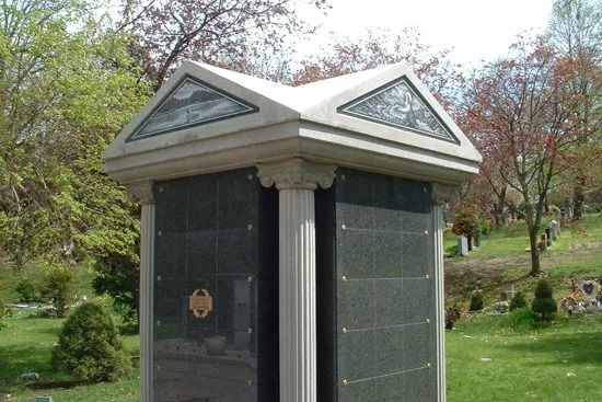 Small black memorial structure with a white roof in a grassy cemetery garden