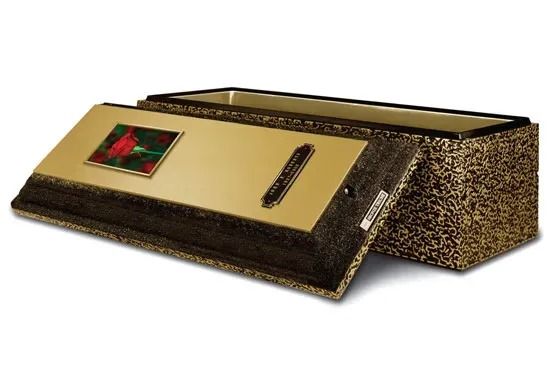 Gold rectangular box with a patterned side, lid open beside it, and a small colorful label on top