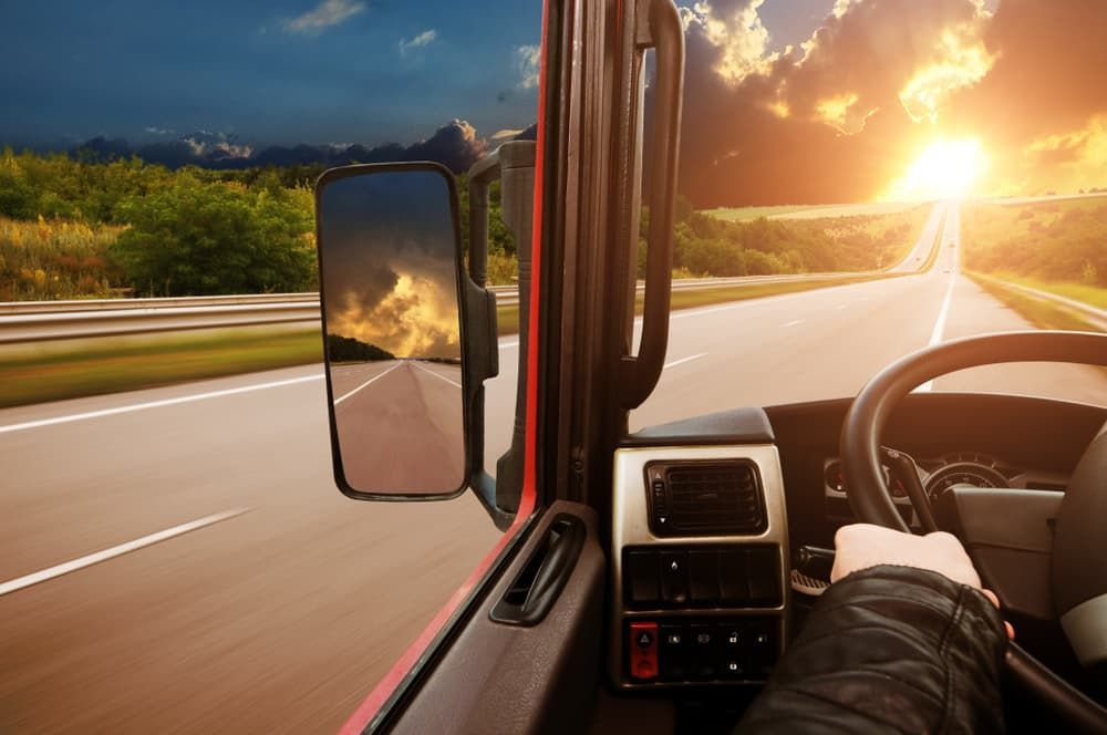 A truck driver is driving down a highway at sunset. — Petrena Windscreens In Highfields, QLD