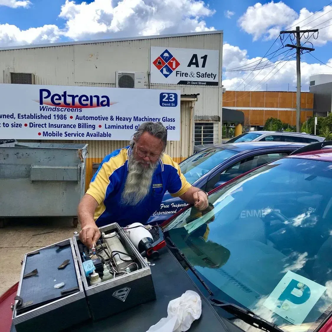 A Man With A Beard Is Working On The Windshield Of A Car — Petrena Windscreens In Oakey, QLD