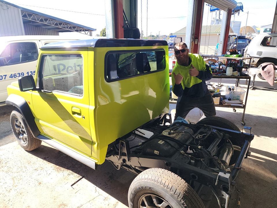 A Man Is Working On A Yellow Truck In A Garage — Petrena Windscreens In Crows Nest, QLD