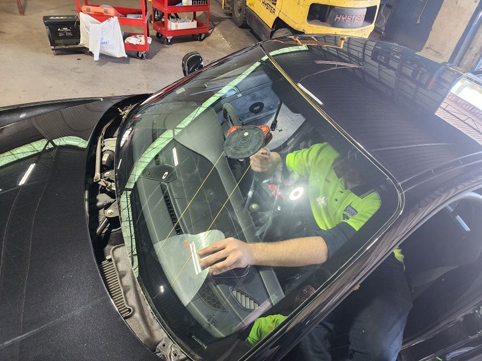 A Man Is Cleaning The Windshield Of A Car In A Garage — Petrena Windscreens In Toowoomba City, QLD