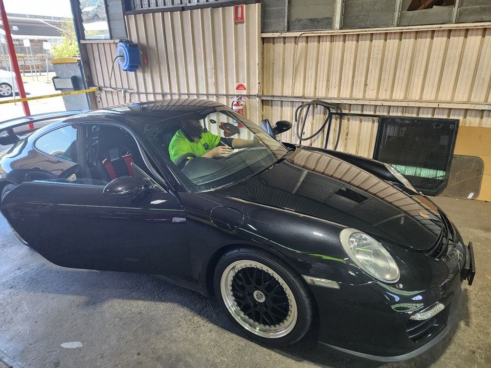 A Man Is Driving A Black Sports Car In A Garage — Petrena Windscreens In Plainland, QLD