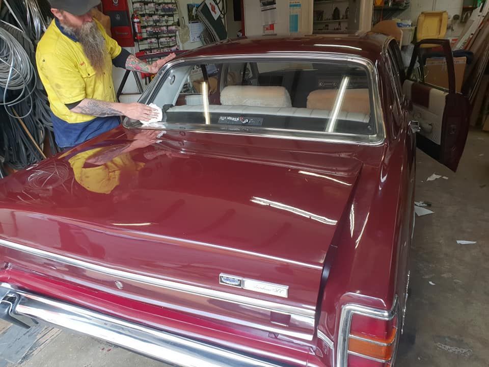 A Man Is Working On A Red Car In A Garage — Petrena Windscreens In Aubigny, QLD