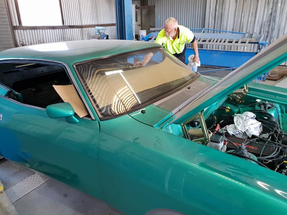 A Man Is Working On A Red Car In A Garage — Petrena Windscreens In Meringandan, QLD