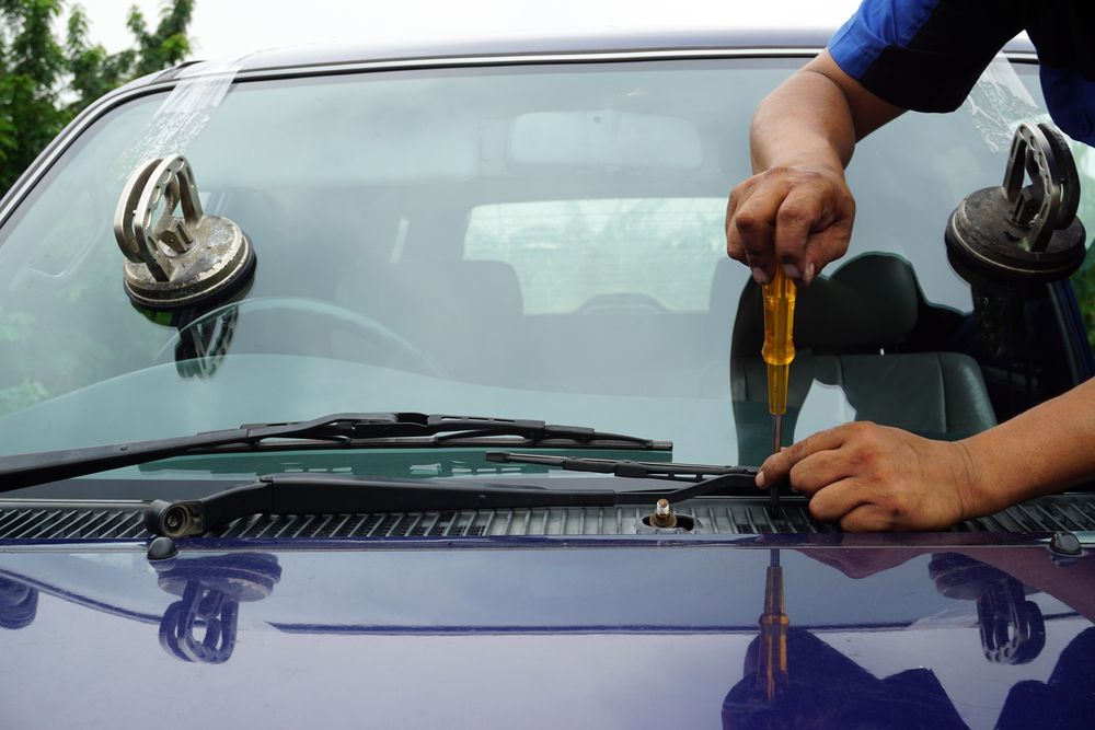 A Man Is Fixing A Windshield On A Car With A Screwdriver — Petrena Windscreens In Plainland, QLD