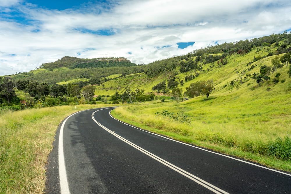 A Curvy Road Going Through A Lush Green Valley With Mountains In The Background — Petrena Windscreens In Clifton, QLD