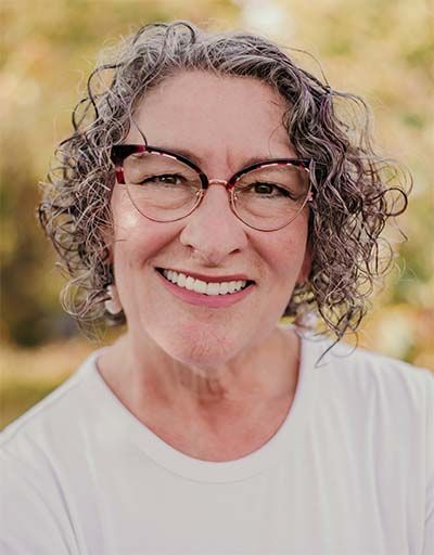 Woman smiling, wearing glasses, and white shirt.