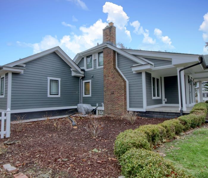 A large gray house with a brick chimney and a porch.