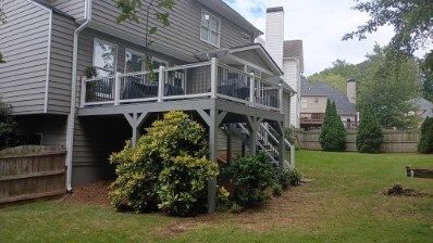 Back of a house with a two-level gray deck. Shrubs in front, green yard, wooden fence.