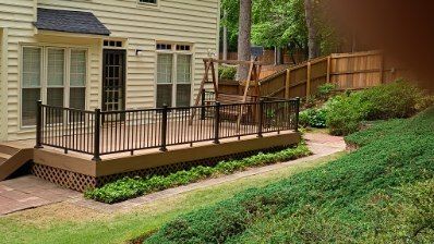 Deck with black railing next to a house with a swing set and a wooden fence on a sloped yard.
