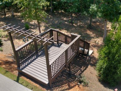 Wooden deck with railing and pergola in a wooded backyard setting.
