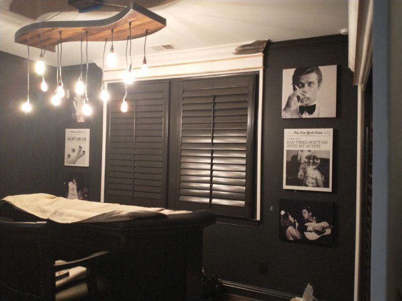 Dark room with black shutters, a table, and celebrity album art on the wall. A unique light fixture hangs from the ceiling.
