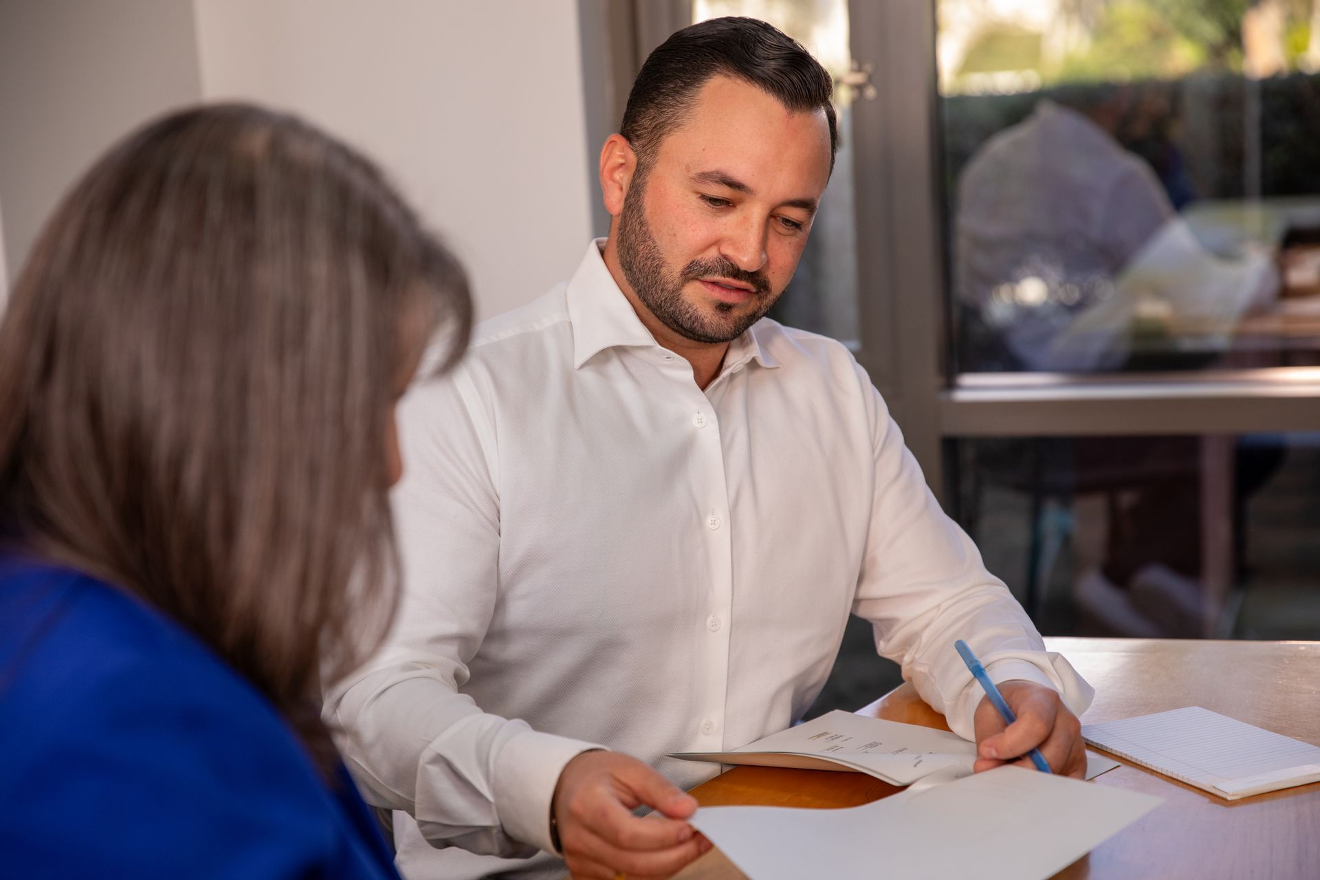 Two people reviewing documents at a table in an office, with one holding papers and a pen.