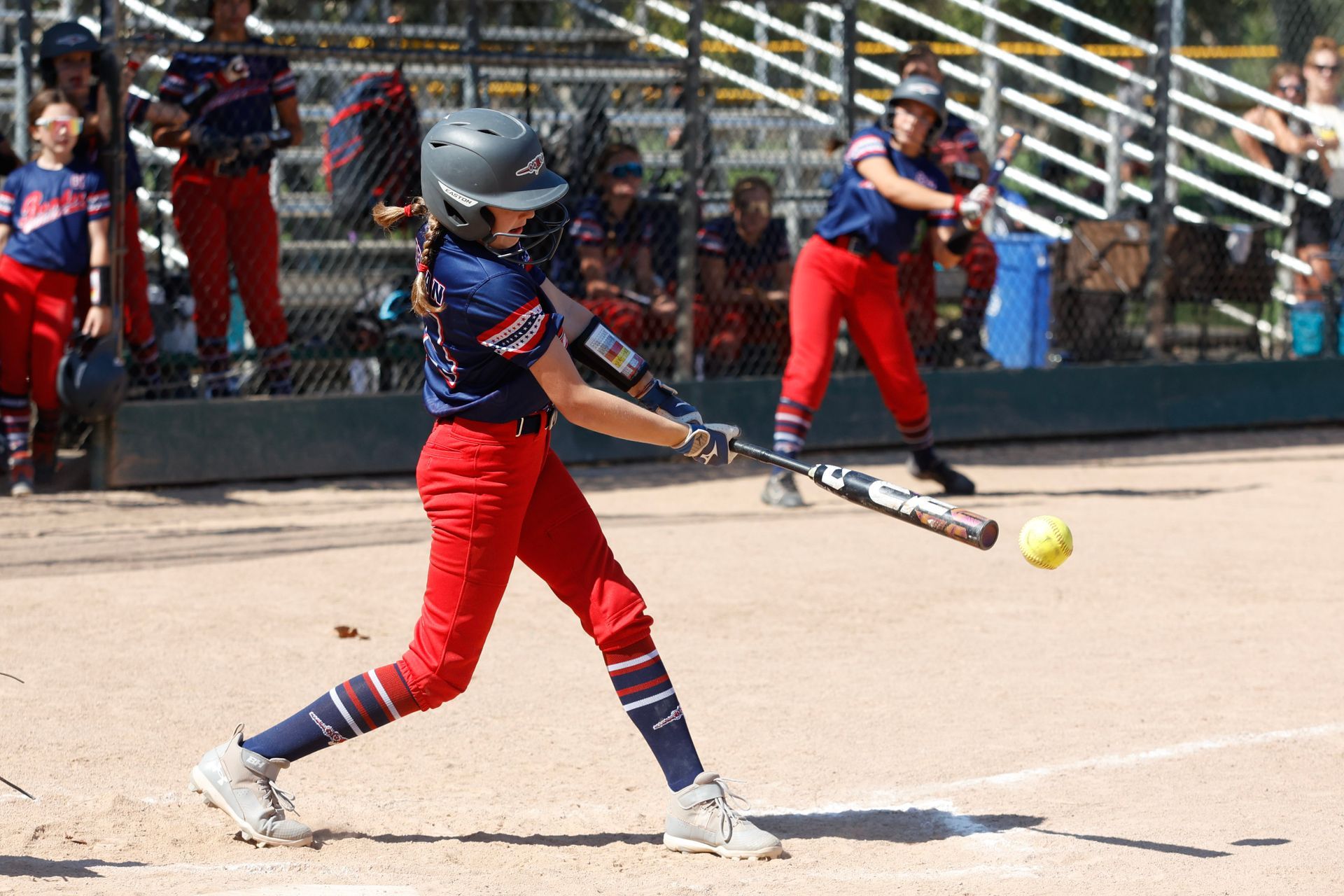 A girl is swinging a bat at a ball while playing softball.